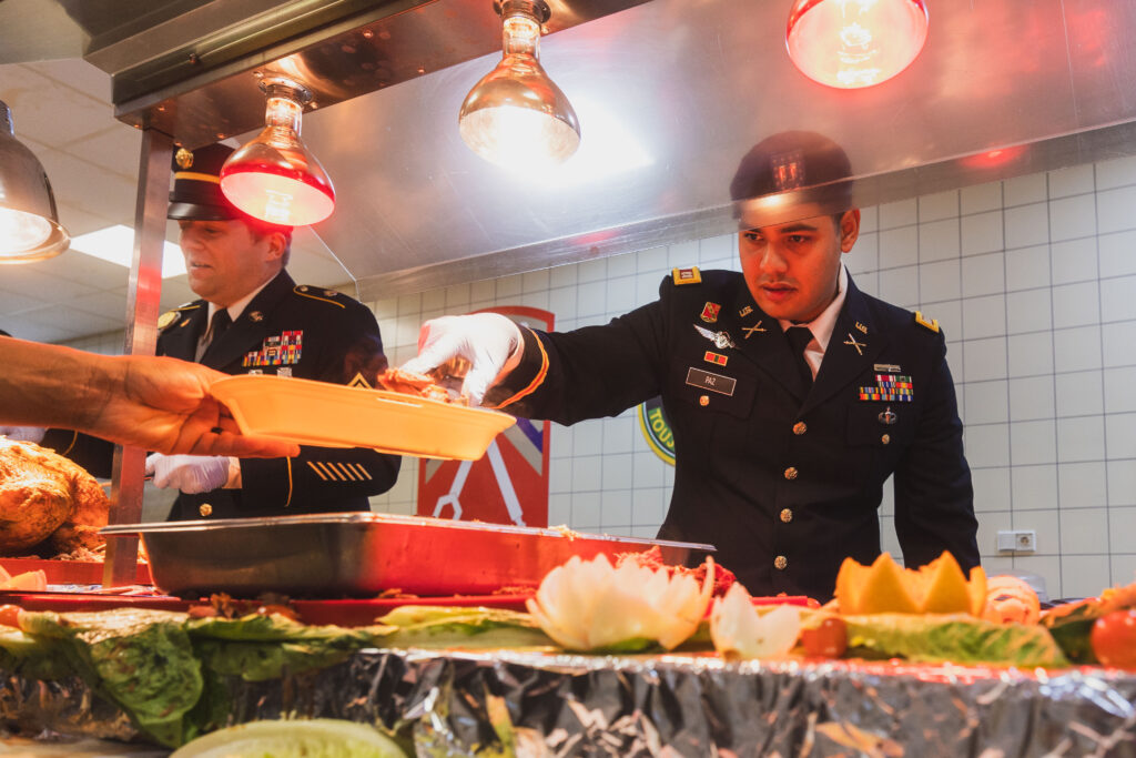 Mitglieder des Führungsteams des Headquarters des 7. Ausbildungskommandos der Armee (7th Army Training Command - 7ATC), Capt. Adolfo Paz (rechts) und 1st Sgt. Joshua Taylor, servieren U.S.-Soldaten, Zivilisten und deutschen Staatsangehörigen Essen während der Thanksgiving-Feier des 7ATC in der DAFC in Grafenwöhr. -- Bild: Spc. Christian Carrillo