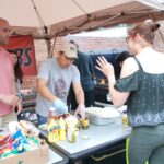 Air Force Maj. Timothy O'Rourke (left), director of operations for the 424th Air Base Squadron, and Tech. Sgt. Daniel Kim (center), assigned to the 424th Air Base Squadron, sold barbecue during the American Festival, June 17, 2018, in Chièvres, Belgium.
