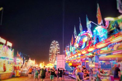 Belebtes Deutsch-Amerikanisches Volksfest Grafenwöhr bei Nacht mit Fahrgeschäften und einem beleuchteten Riesenrad im Hintergrund. — Bild: volksfest-grafenwoehr.de